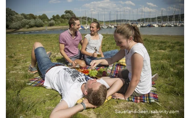 Eine Gruppe Jugendlicher entspannt auf der Liegewiese am Seeufer