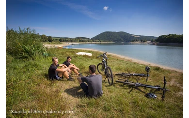 Eine Gruppe Jugendlicher macht Pause auf einer Wiese am See