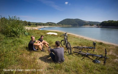 Eine Gruppe Jugendlicher macht Pause auf einer Wiese am See